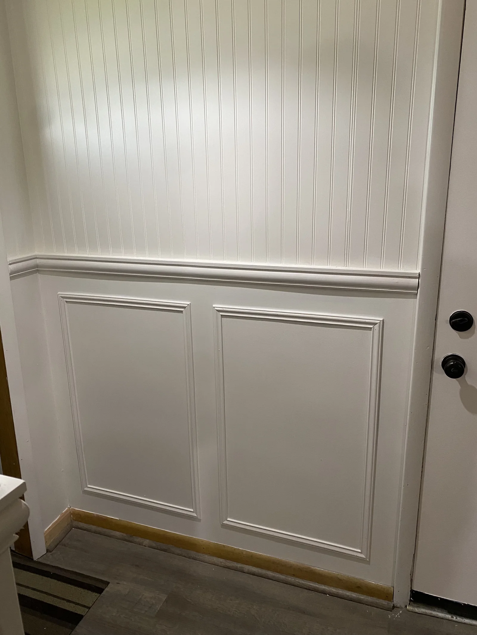 Detail of white beadboard and panel moulding beside an interior door