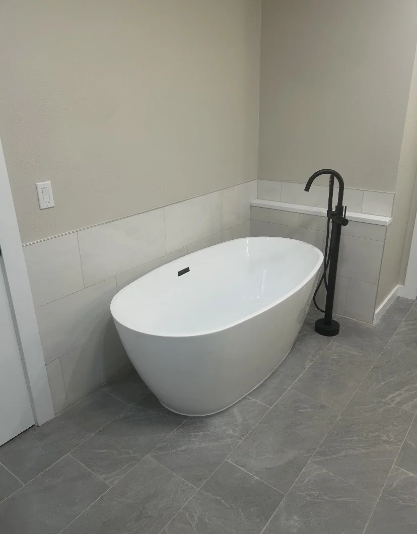 Freestanding white bathtub with dark floor-mounted faucet